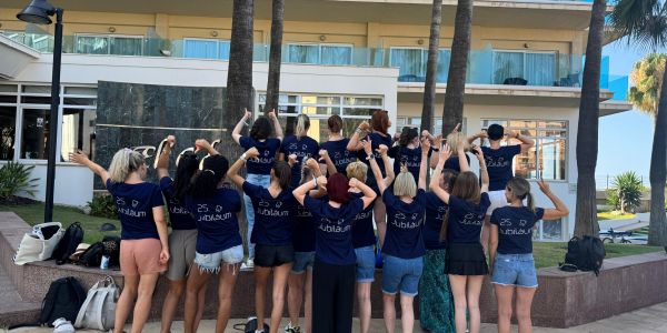 Das Praxisteam steht gemeinsam vor dem Hotel, alle mit dem Rücken zum Fotografen, die Hände in der Höhe. Alle tragen